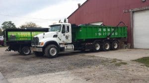 A white truck with a large green dumpster attached is parked beside a red building. Another black truck with green signage, also advertising "Junk Raps," is parked nearby. Both vehicles display a junk removal service number.